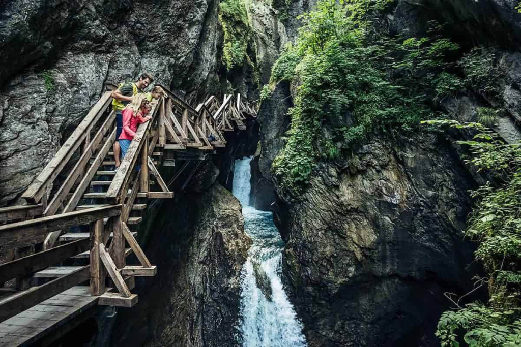 Holzsteig in einer engen Schlucht mit Personen über einem Wasserfall