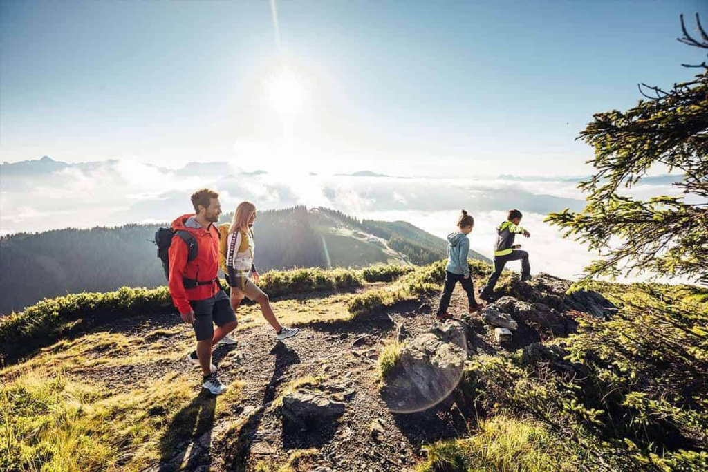 Vier Personen wandern auf einem sonnigen Bergpfad mit Blick auf nebelbedeckte Täler