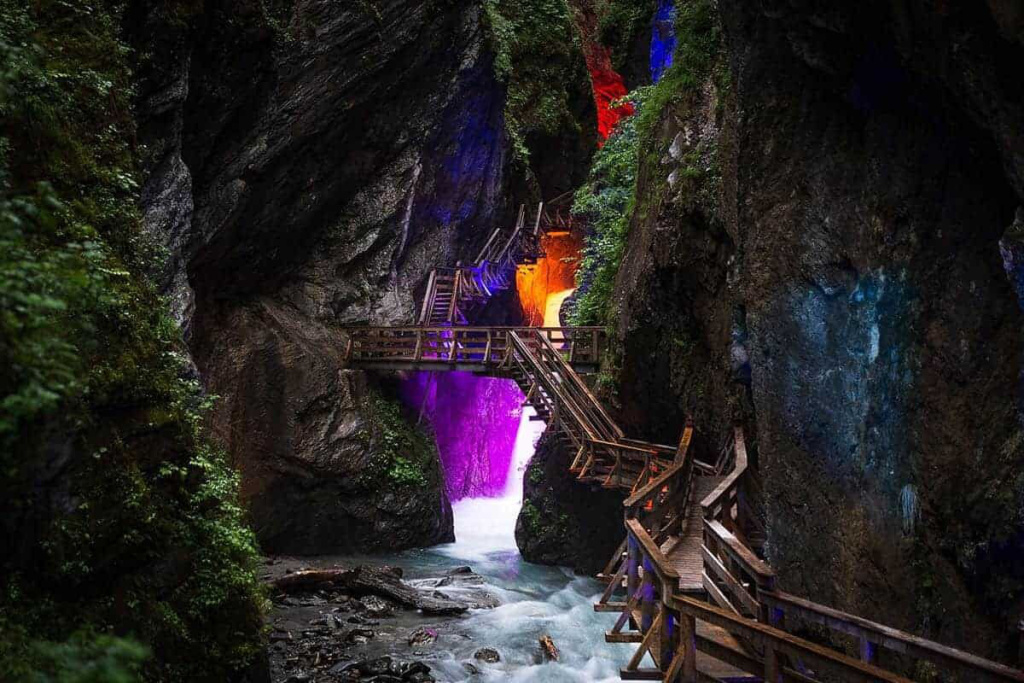 Holzstege in einer schmalen Schlucht mit farbig beleuchtetem Wasserfall